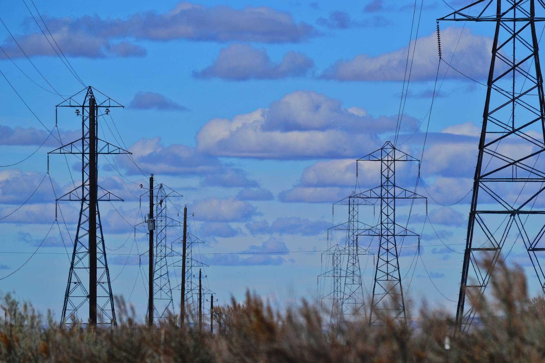 Sun setting behind high-voltage power lines and electricity pylons in a rural landscape.