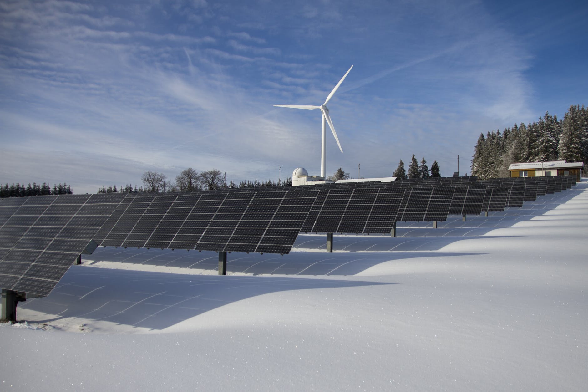 Large scale solar panels and wind turbines under a blue sky representing renewable energy assets.