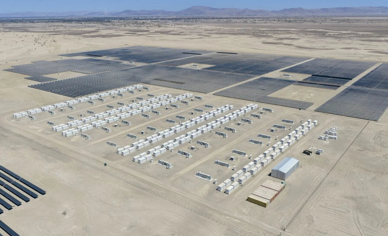 Massive rows of white battery storage containers next to a large-scale solar PV farm in a desert.