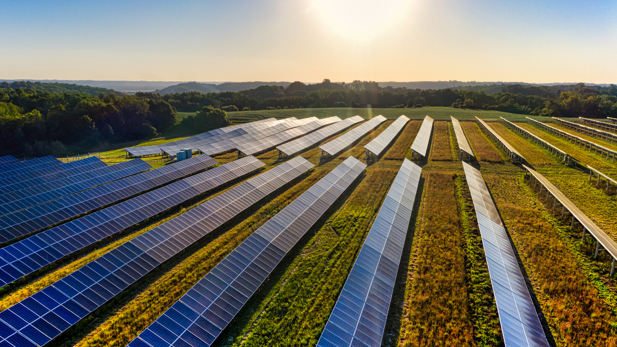 Aerial view of a large-scale solar farm with integrated battery storage containers in a Mediterranean landscape.