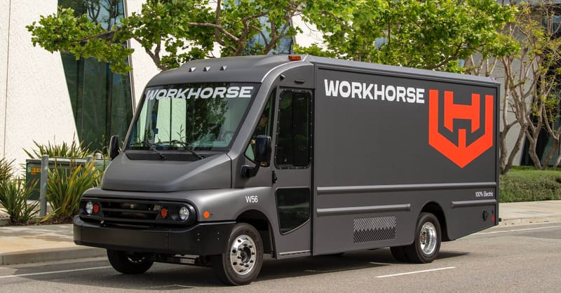 A heavy-duty electric truck charging at a commercial logistics hub with solar panels on the warehouse roof.