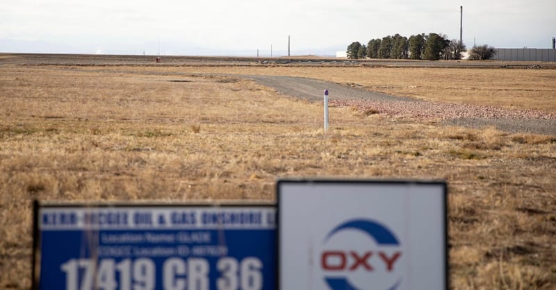 Industrial drilling rig operating at night near a natural gas processing facility in Colorado.