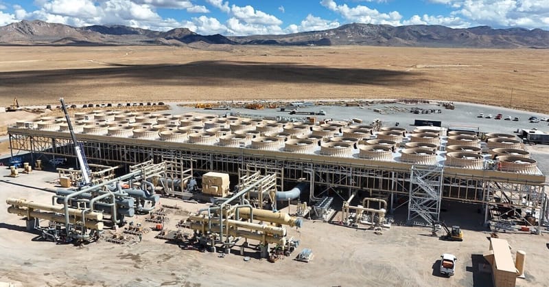 A geothermal power plant facility with steam rising against a clear blue sky