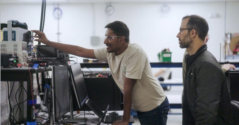 An electrical transformer on a utility pole with a solar panel array in the background