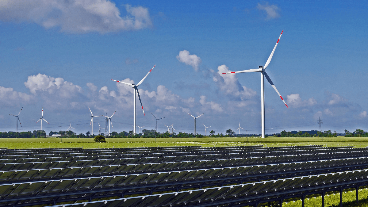 Aerial view of a large-scale solar farm integrated with wind turbines in a mountainous landscape.