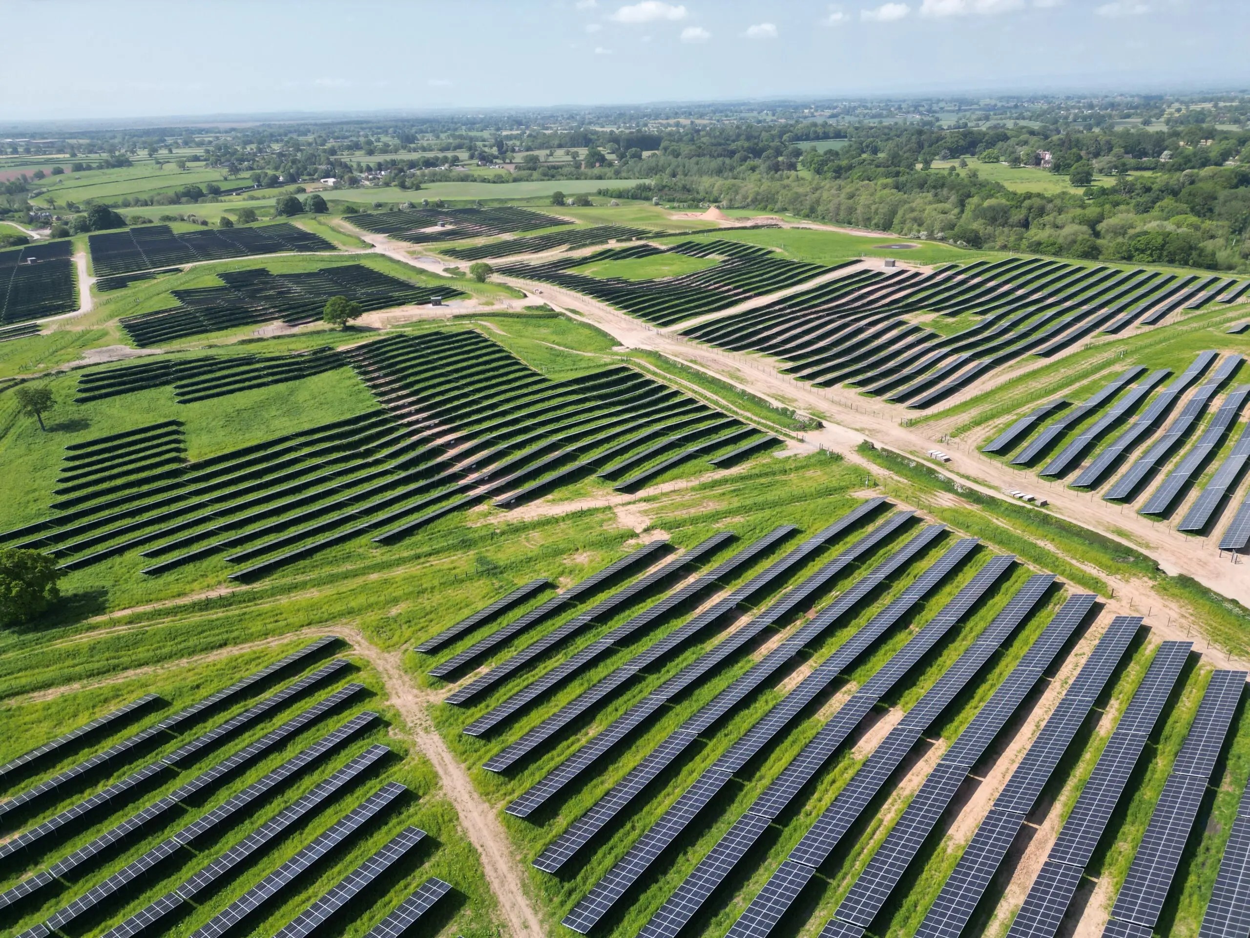 Large scale solar panels being installed alongside battery energy storage containers in a rural field.