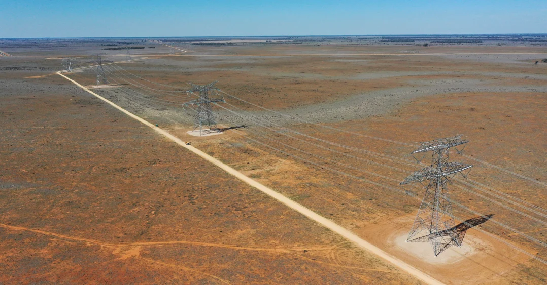 Large scale transmission towers crossing a dry landscape under a clear blue sky.