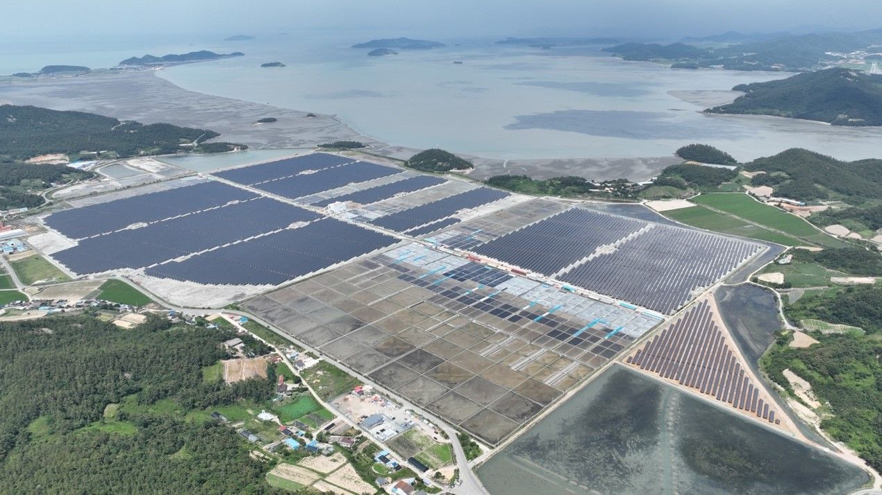 Aerial view of a large-scale solar panel farm with rows of photovoltaic modules under a clear blue sky.