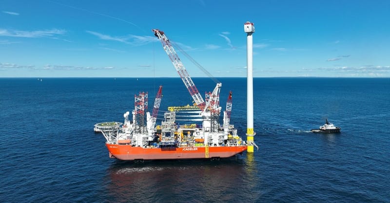 Large offshore wind turbine construction vessel operating in the ocean with clear blue skies.