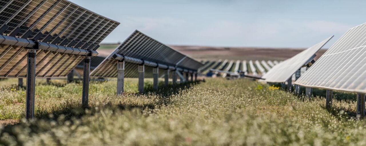 Aerial view of a massive solar farm integrated with containerized battery storage units near an industrial facility.