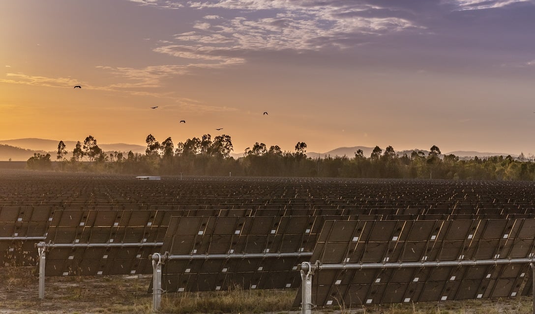 Aerial view of a large-scale solar farm integrated with battery storage containers in a rugged industrial landscape.