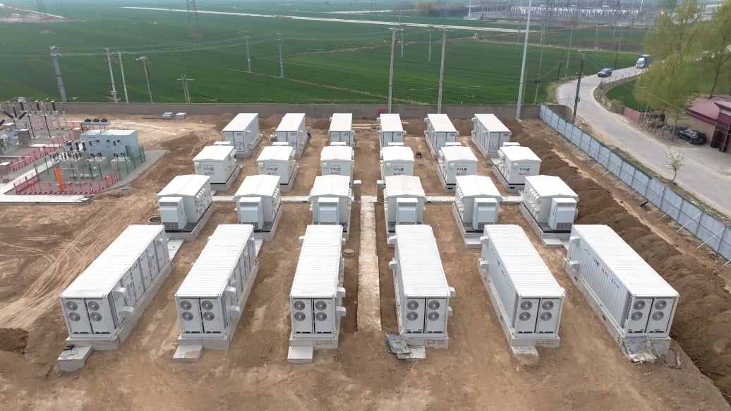 A row of large-scale industrial battery energy storage containers at a solar farm site.