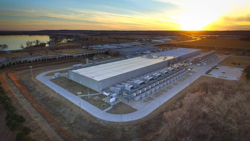A massive grid-scale BESS installation with white battery containers and solar panels in the background.