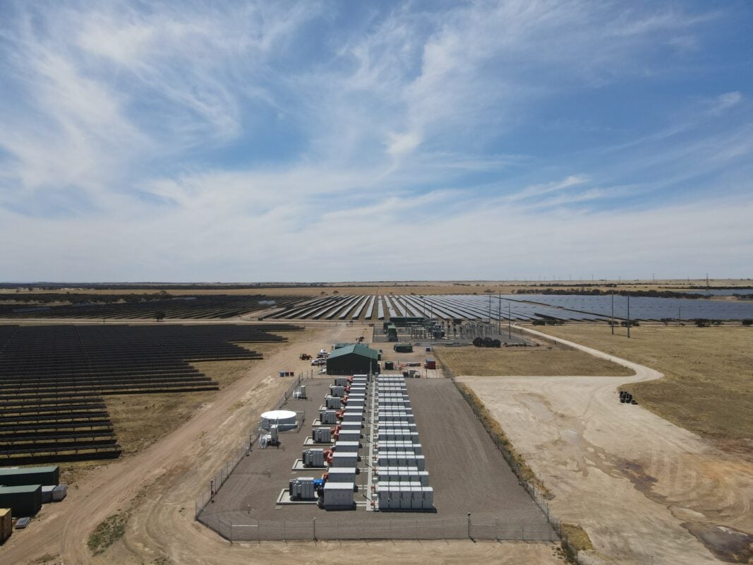Aerial view of a massive solar array integrated with rows of containerized battery energy storage systems