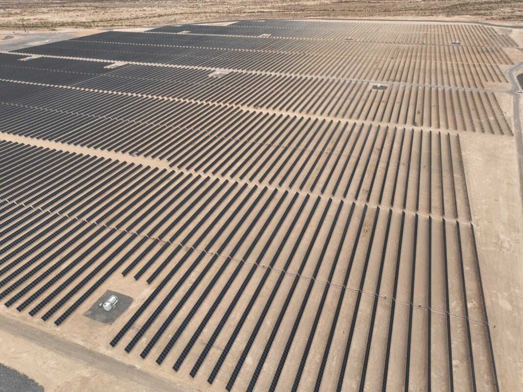 Aerial view of a large-scale solar farm under construction in a hilly, forested landscape