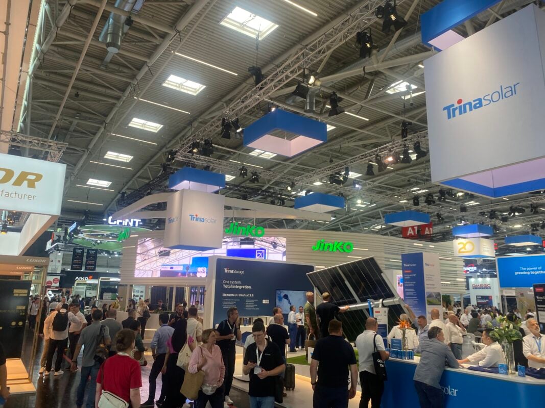 A wide shot of solar professionals walking through the crowded but somber halls of Messe München.