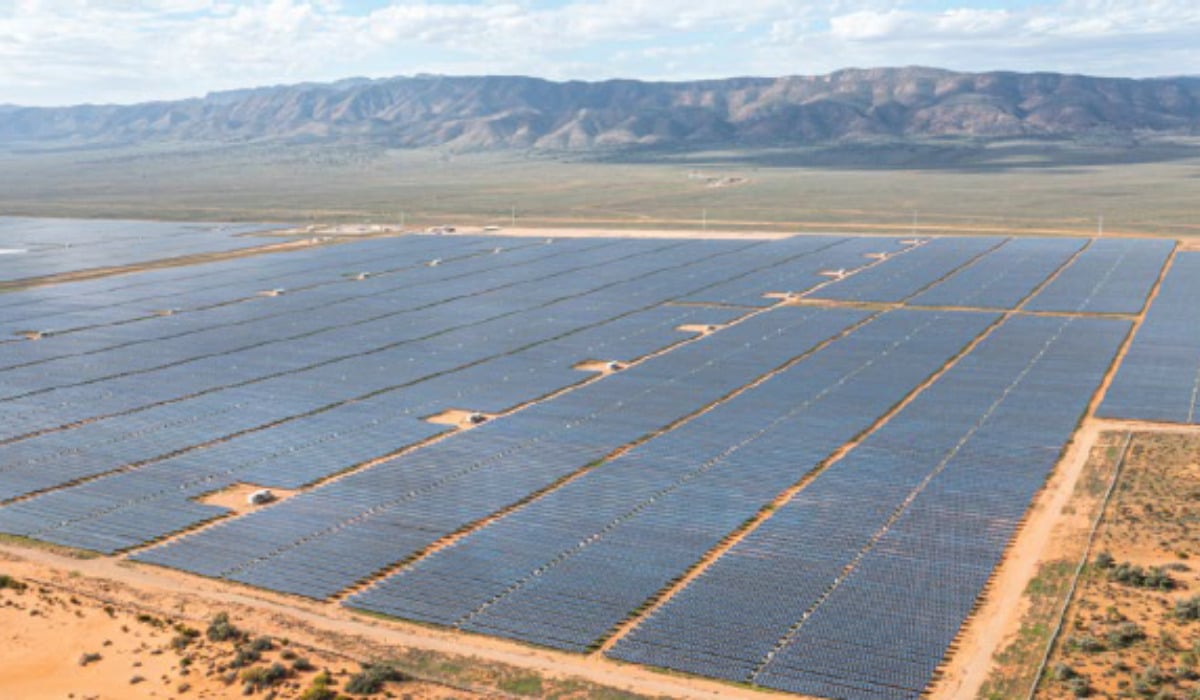 Aerial view of a large-scale solar farm and wind turbines in the South Australian landscape under a clear blue sky.