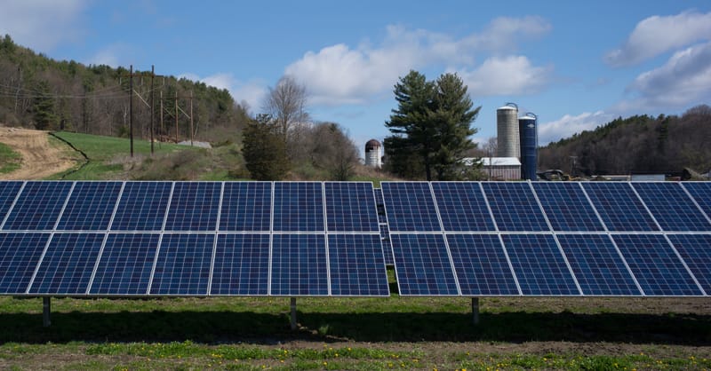 A split-view image showing solar panels installed above active farmland in a rural European setting.