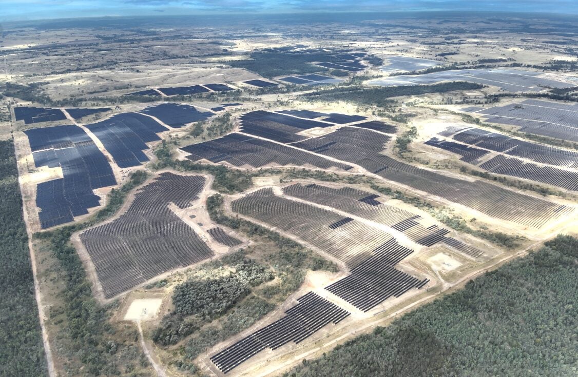 Large scale solar farm integrated with rows of containerized battery energy storage systems in a dry landscape.