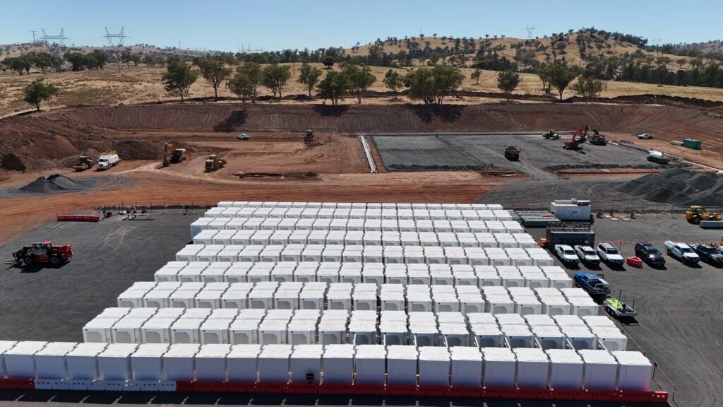 Large-scale battery storage containers lined up in a grid formation with electrical infrastructure.
