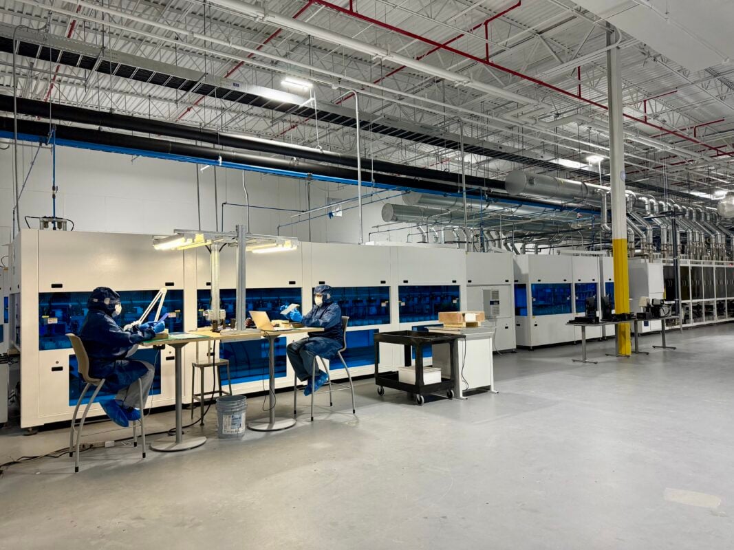 Aerial view of a massive solar module assembly factory with empty storage racks.