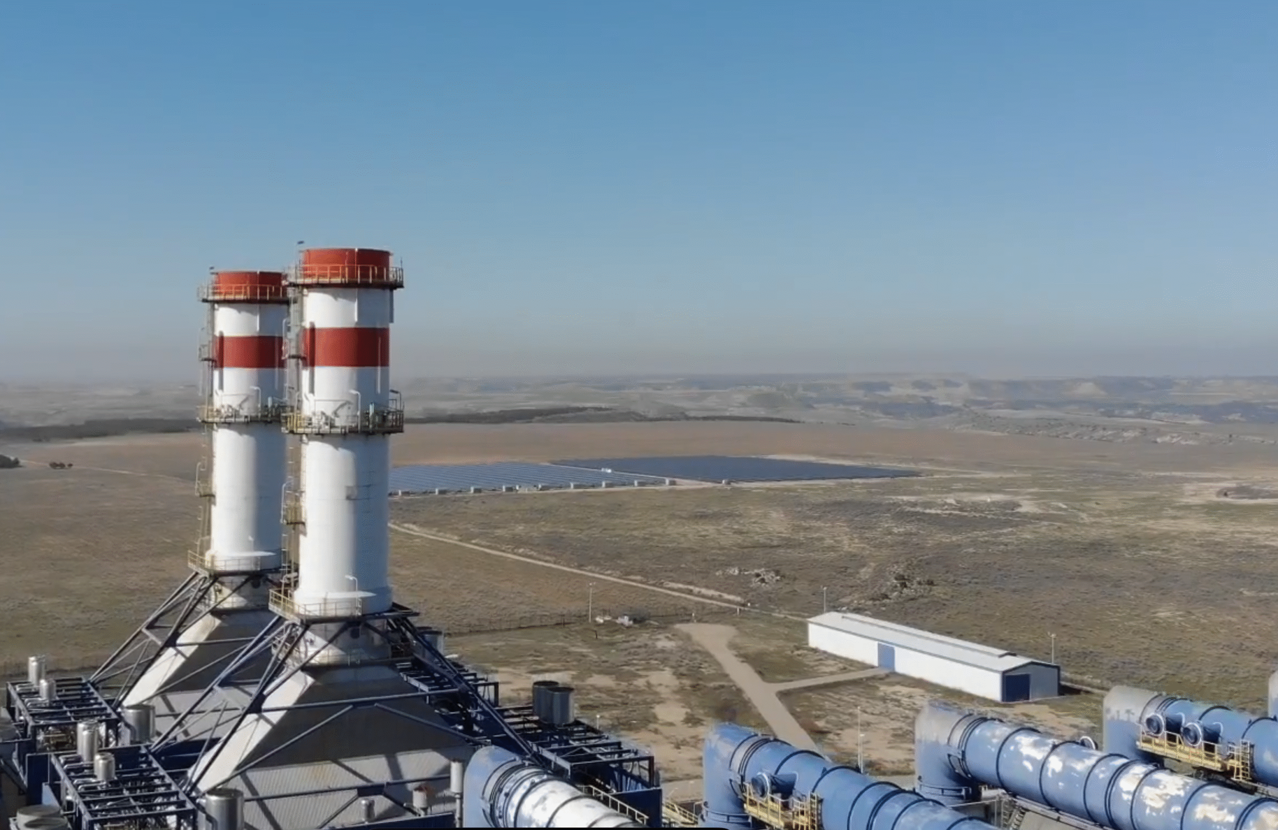 Aerial view of a large-scale solar array integrated near a thermal power station infrastructure