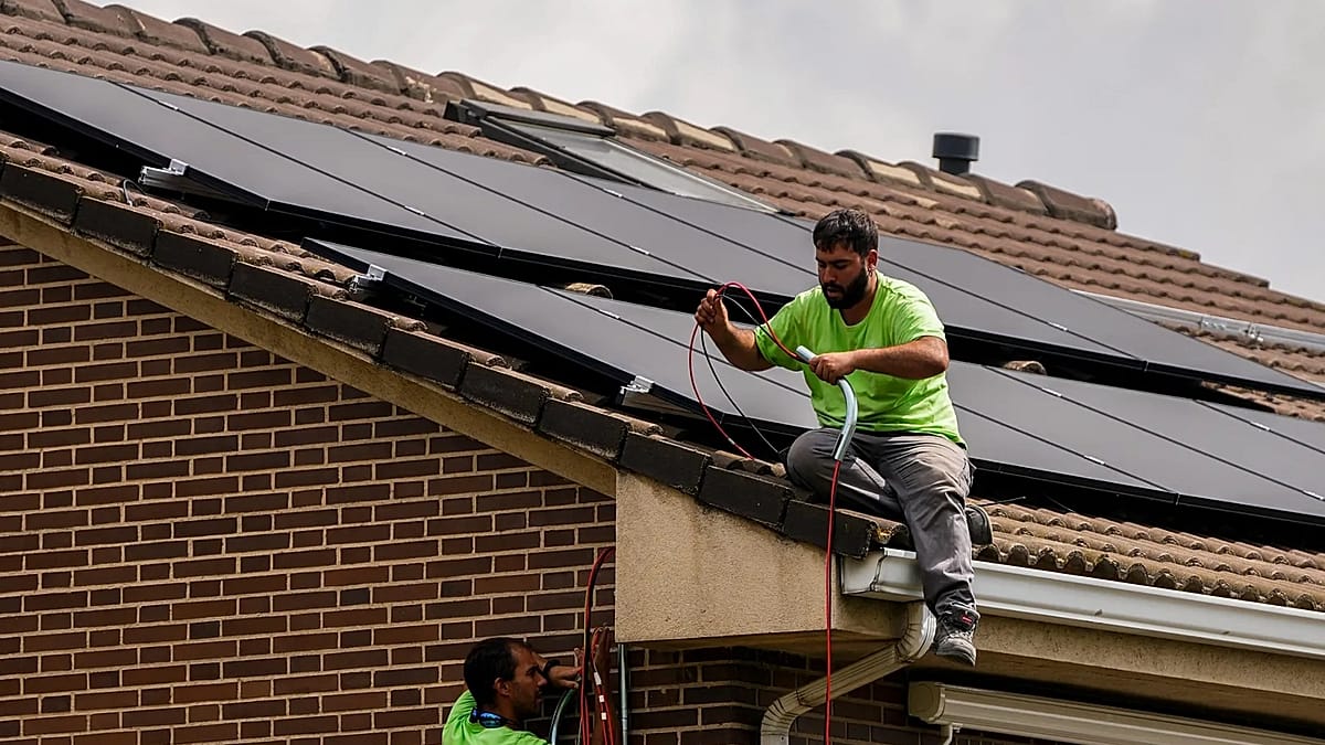 A row of residential solar panels on rooftops under a clear European sky.