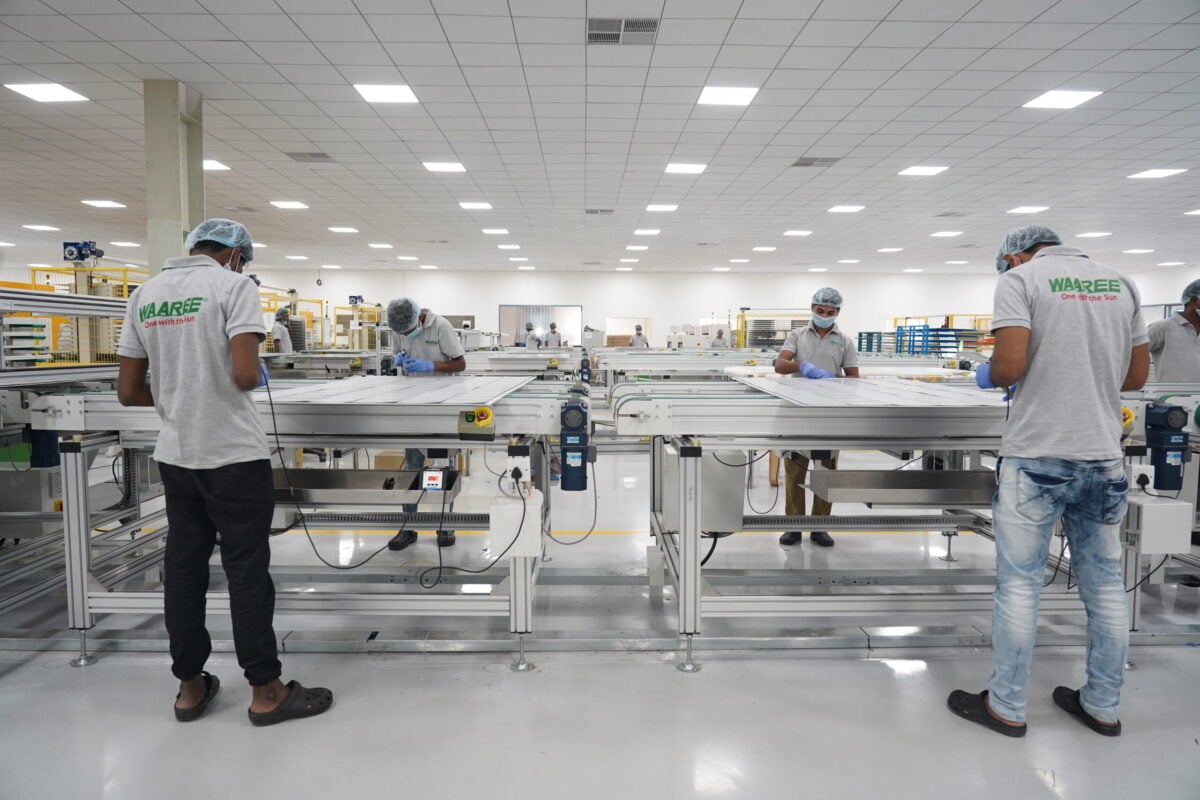 Exterior view of a large, modern solar panel manufacturing facility with rows of machinery.