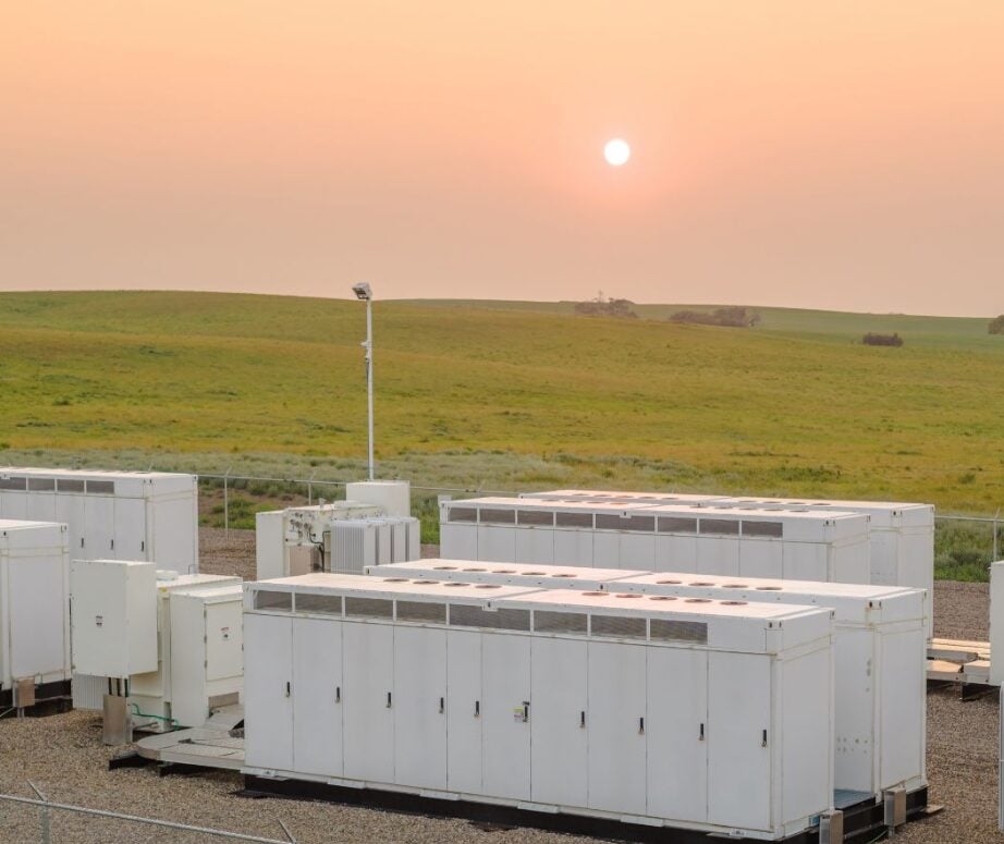 A large-scale lithium-ion battery energy storage system facility under a bright blue sky.