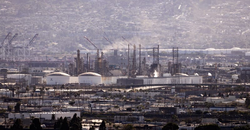 Large industrial facility with solar panels in the foreground under a hazy sky.