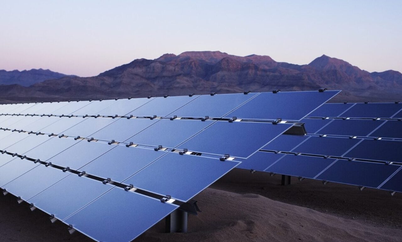 Large scale solar farm with thousands of panels stretching to the horizon under a clear sky