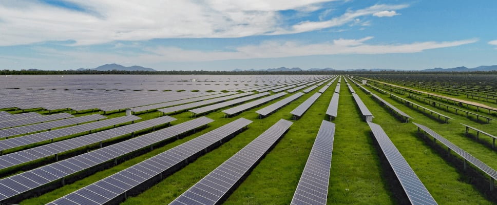 Aerial view of a massive solar array and wind turbines across the Australian landscape.