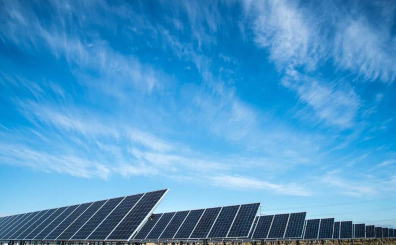 A vast utility-scale solar farm reflecting the sky under a bright sun