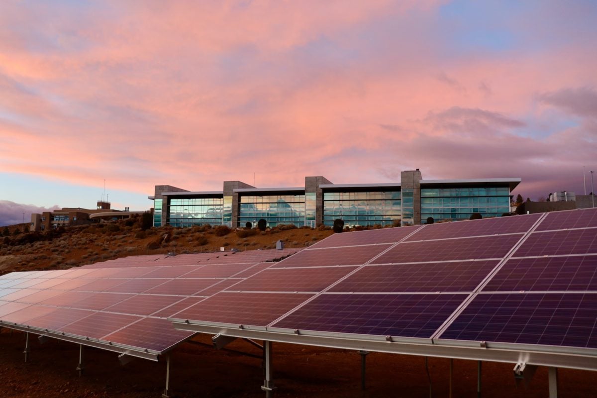 A grid-scale battery storage container situated next to a utility-scale solar farm under a clear sky.