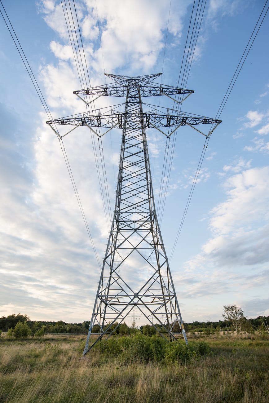 A high-voltage transmission pylon silhouetted against a bright sky, representing grid infrastructure.
