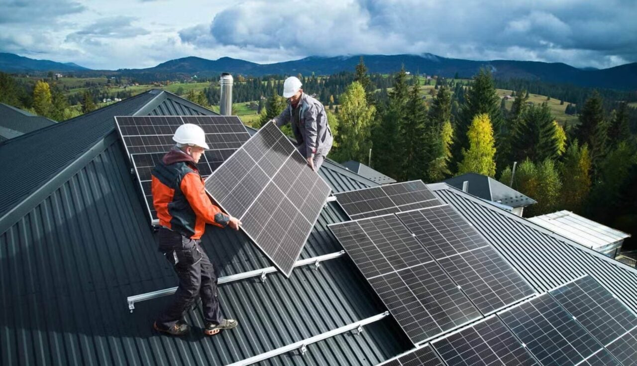 A modern solar inverter being installed on a residential wall with a digital interface