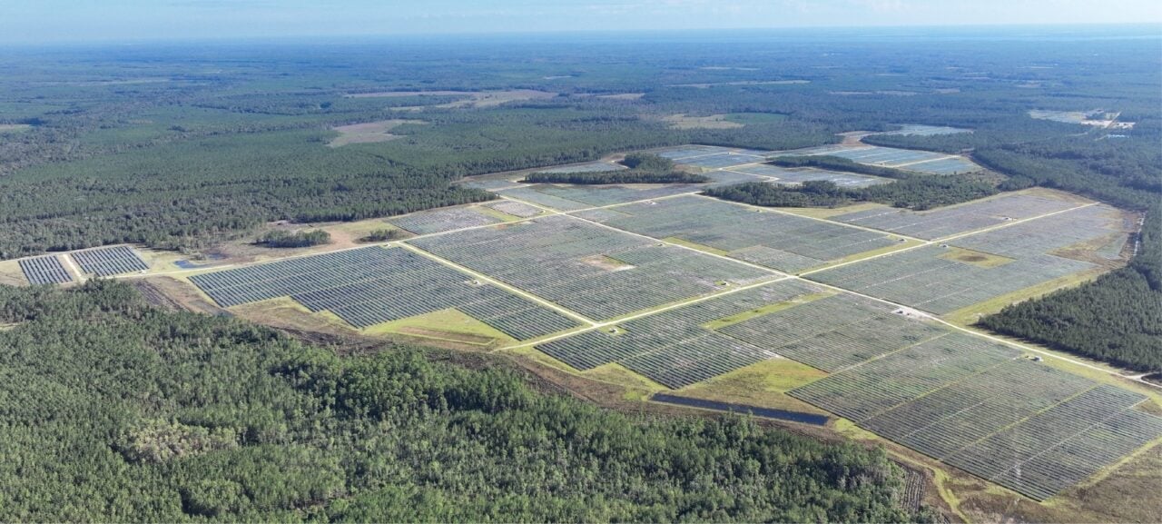 A large-scale solar farm with integrated battery storage containers under a clear blue sky.