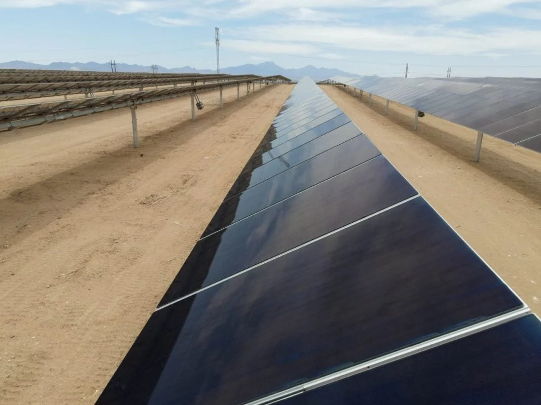 Aerial view of a massive solar farm interconnected with high-voltage utility transmission lines.