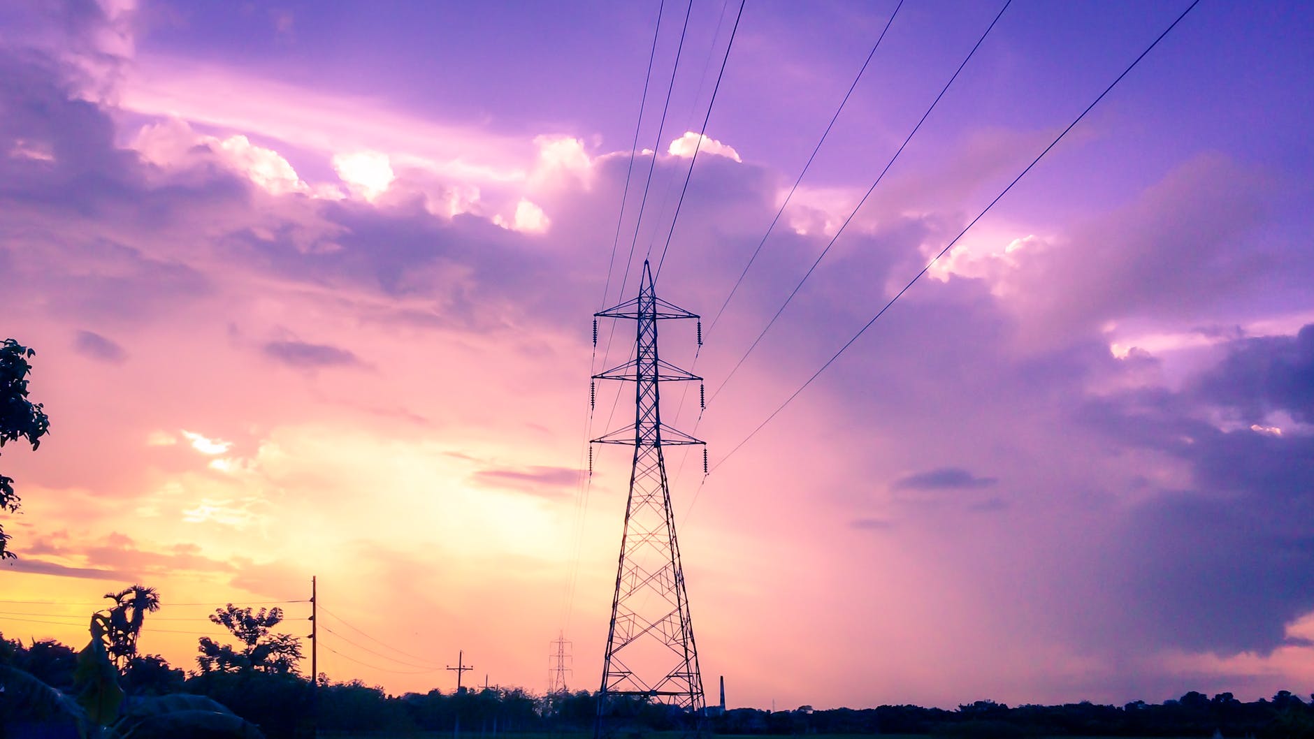 Large high-voltage electricity pylons silhouetted against a hazy, orange-red sun during a severe urban heatwave.