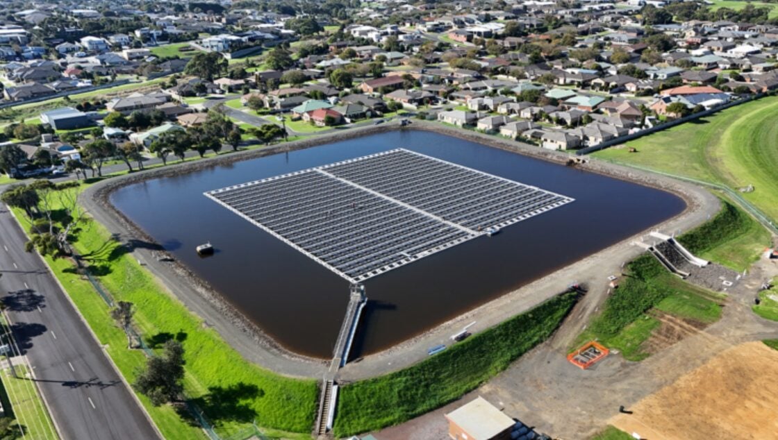 A large-scale floating solar array on a freshwater reservoir with blue water and mountains.