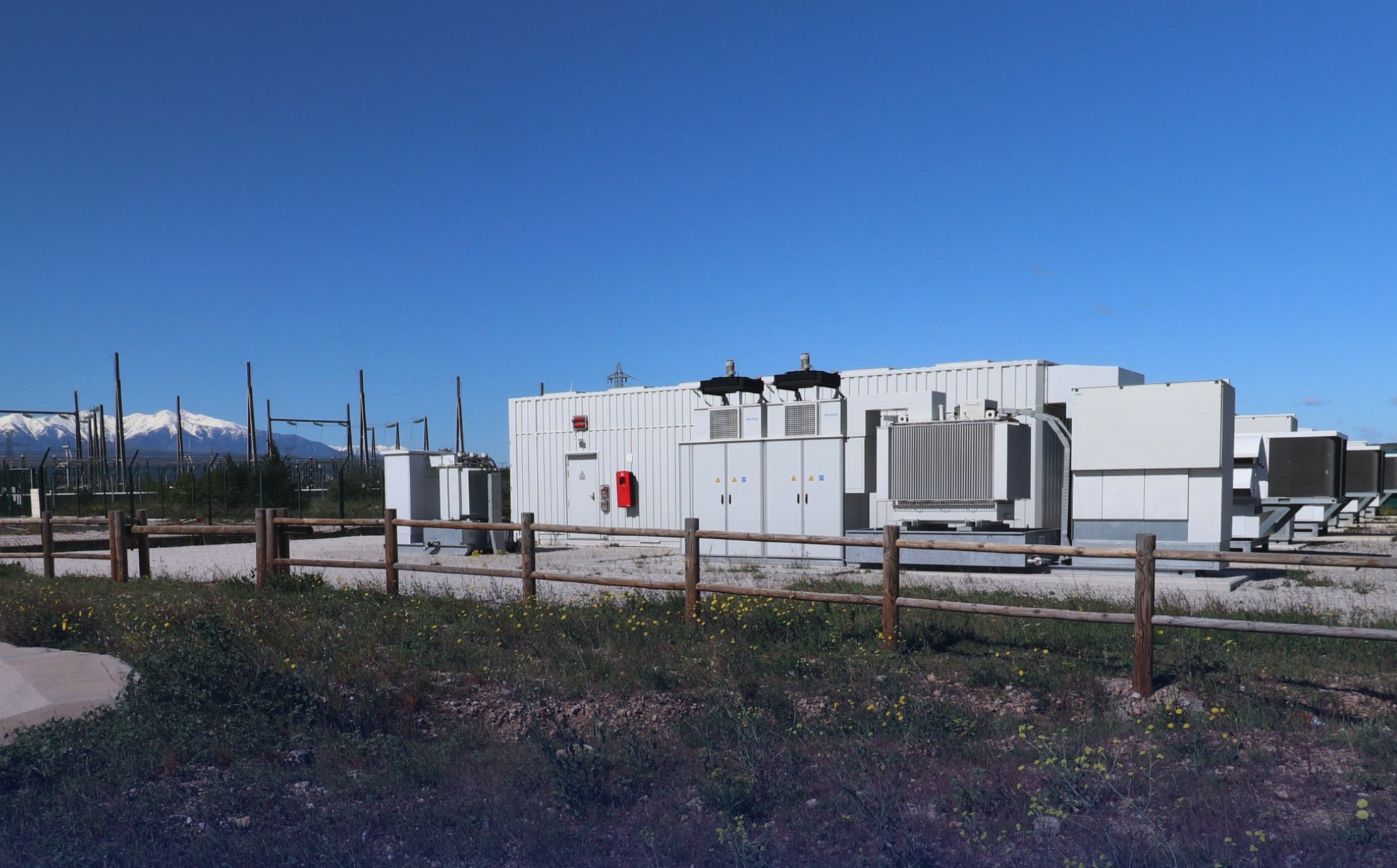 Industrial scale battery containers located near a mountainous hydroelectric dam facility.