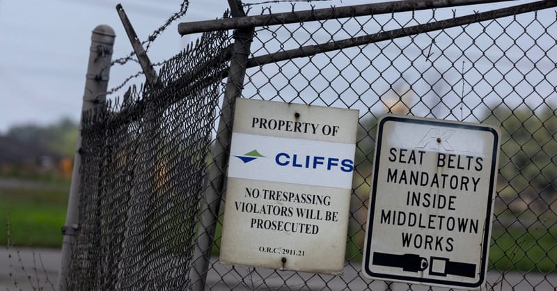 Industrial steel mill smokestacks emitting smoke next to a large-scale commercial solar array.