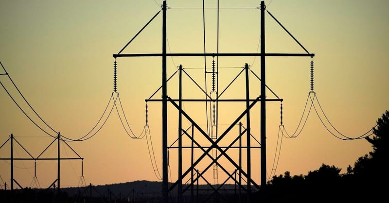 High-voltage transmission towers stretching into a forested horizon under a cloudy sky.