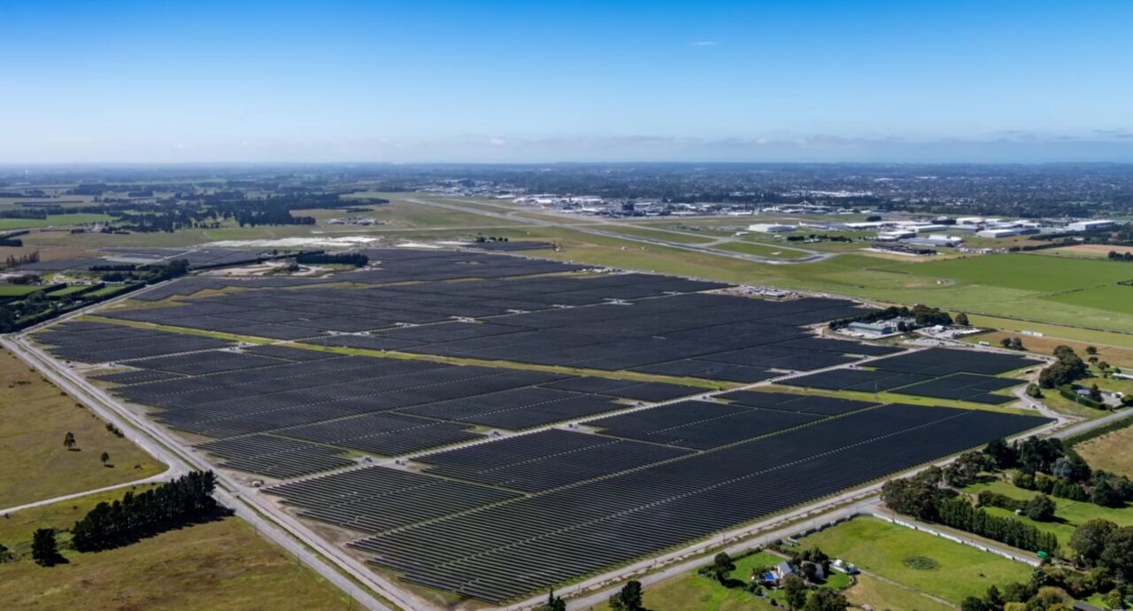 Large scale solar array installed on flat land adjacent to an airport runway and hangar facilities.