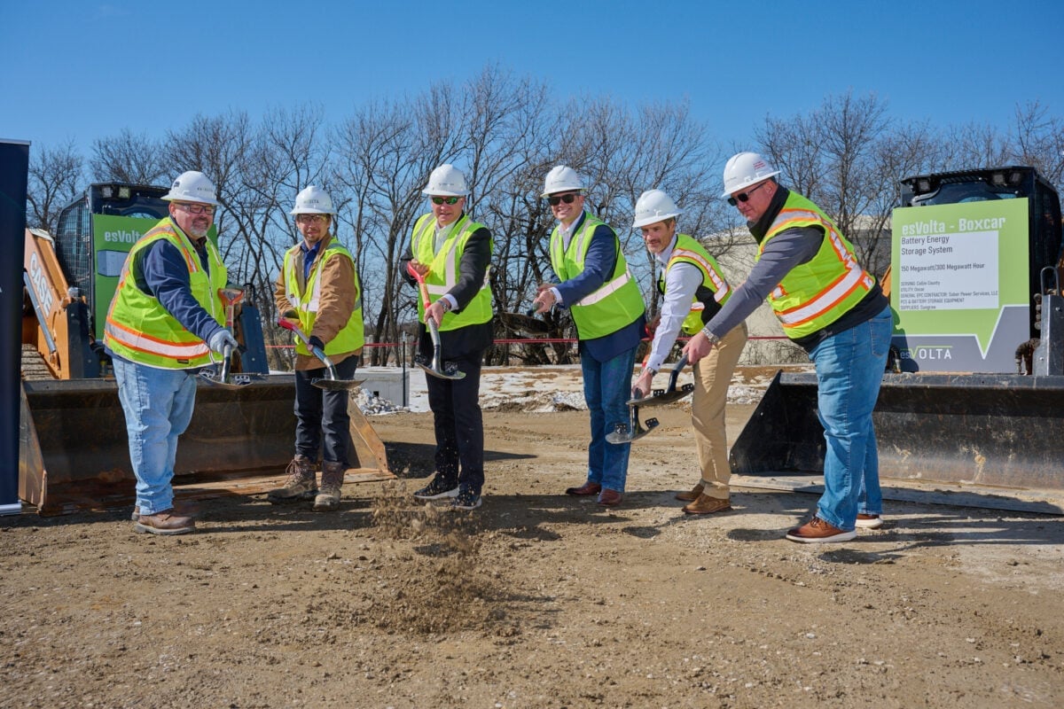 A large-scale grid battery energy storage system (BESS) installation in a sunny, open field.