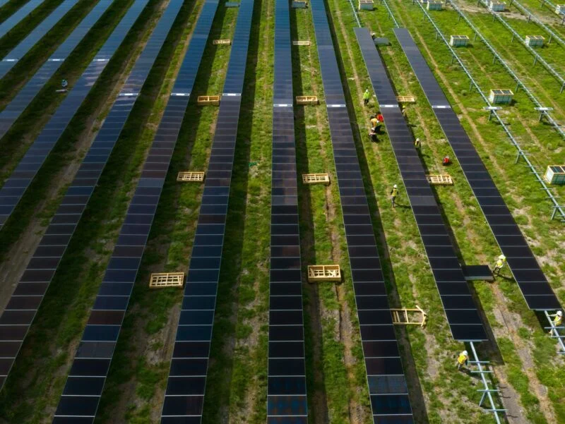 Aerial view of a utility-scale solar farm under construction in a rolling green landscape.