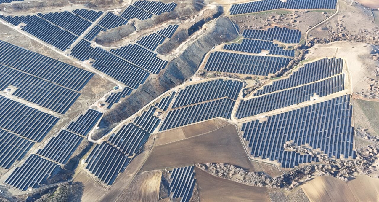 Aerial view of a massive solar PV array installed on the rugged terrain of a former Greek lignite mine.