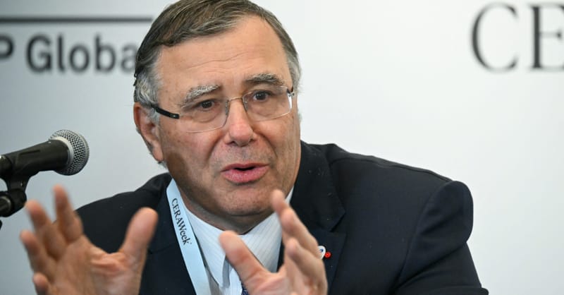 A wind turbine standing in the ocean during sunset with a commercial ship nearby