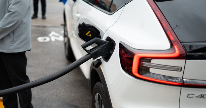 An electric vehicle charging at a large retail store parking lot with solar panels visible on the roof.