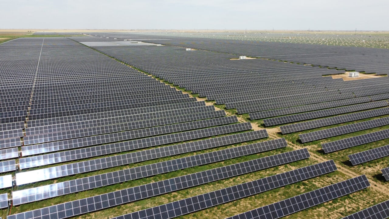 Aerial view of a massive utility-scale solar farm under construction in a dry, flat landscape.